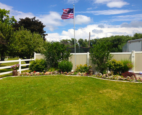 Two-Tone Vinyl Privacy Fence with Gate (on Right) Next to Flower Bed and Flag