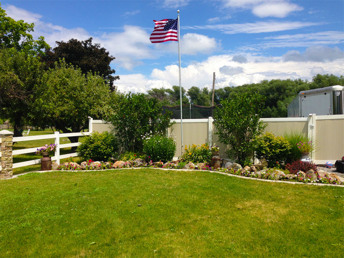 Two-Tone Vinyl Privacy Fence with Gate (on Right) Next to Flower Bed and Flag