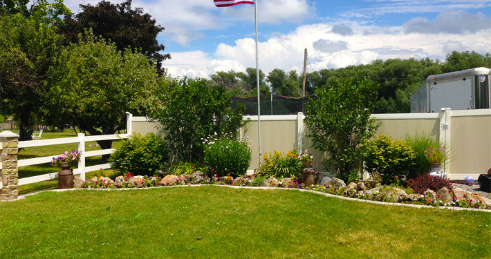 Two-Tone Vinyl Privacy Fence with Gate (on Right) Next to Flower Bed and Flag