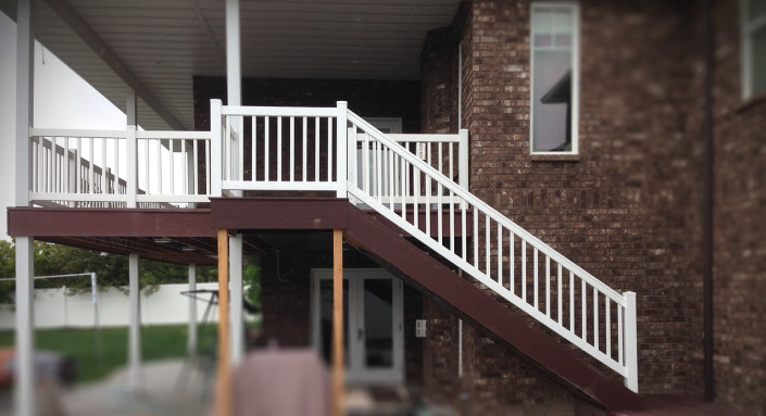 Side view of vinyl handrail on deck stairs of brick house.